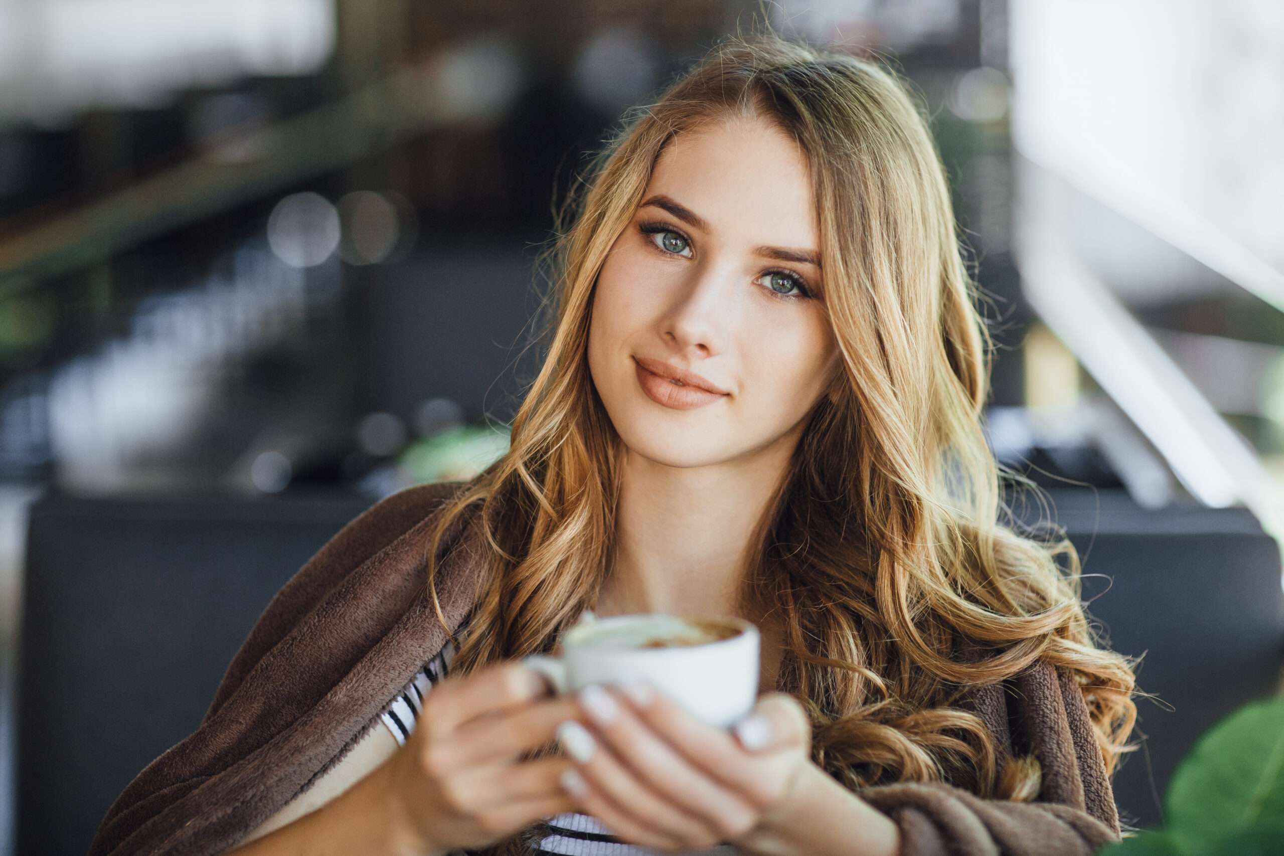 Young pretty girl blonde in casual clothes resting and drinking coffee on a summer terrace cafe. She was presented with a bunch of roses.