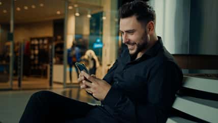 Caucasian stylish man in black suit successful businessman customer sit at shopping mall using mobile phone apps make online order buying clothes win internet discounts chatting distant communication. High quality 4k footage