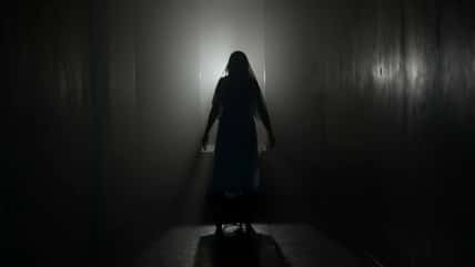 Portrait of ghost female in the house. Woman in white dress with veil covering her face walking in the room with lightning.
