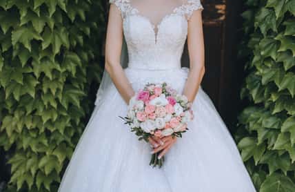 The bride in a white dress holds a wedding bouquet of roses in her hands. Closeup portrait of fresh flowers on nature, against a background of green foliage. Photography, concept.
