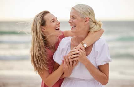 Smile, beach and senior mom with daughter for bonding holiday, love and embrace on weekend travel. Nature, mother and woman laughing on ocean adventure together with hug, fun and island vacation