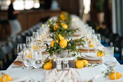 Festive table at the wedding party are decorated with lemon arrangements, on the table are plates with napkins and glasses