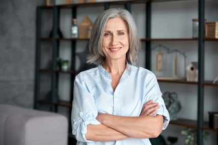 Smiling confident stylish mature middle aged woman standing at home office. Old senior businesswoman, 60s gray-haired lady executive business leader manager looking at camera arms crossed, portrait.