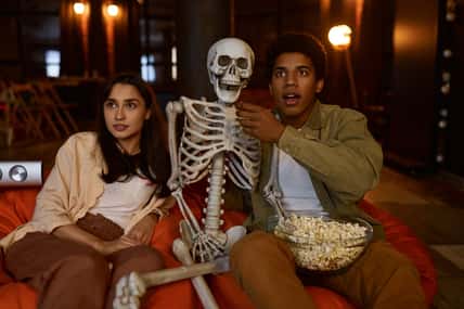 Funny couple and skeleton watching projector. Empty studio interior. Stay at home concept