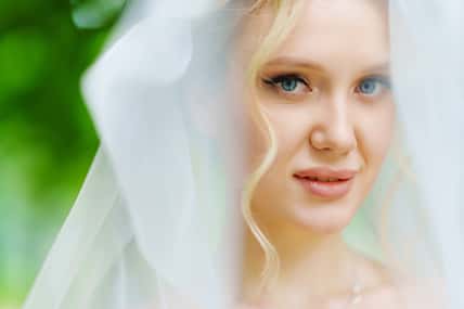 Portrait of a beautiful blonde bride in a veil against the background of green trees. Happy wedding and newlyweds.