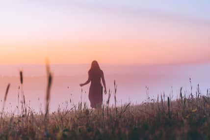 silhouette young woman in a dress walking on a hill on sunrise. female running on a foggy field and enjoying forest landscape. Active life, adventure, freedom, morning, nature concept. dew on grass.