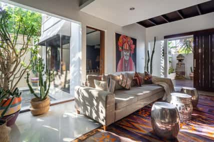 Living room in cozy house with stylish interior, ethnic decor, cushions on comfortable couch, woven ornamental carpet, cactus in wicker basket and artwork on wall