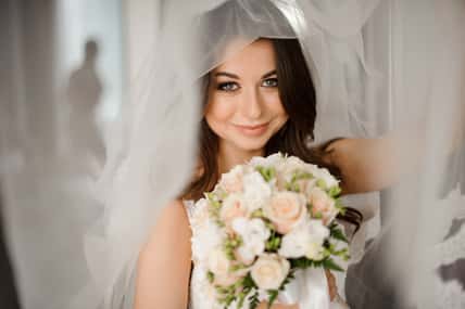 Bride morning preparation. Happy and smiling bride in a white veil holding a lovely wedding bouquet of flowers
