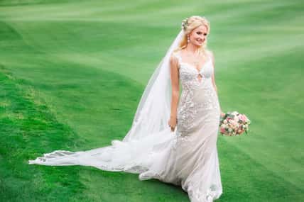 beautiful bride in wedding dress with bouquet of flowers on the green field outdoors