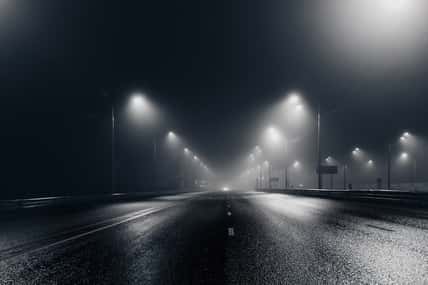 Foggy misty night road illuminated by street lights.
