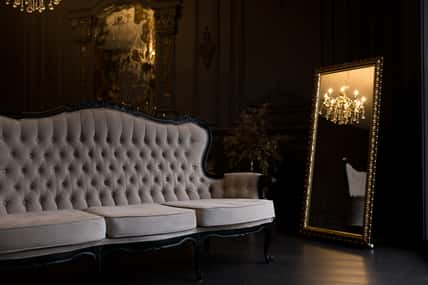 Ancient beige sofa in a dark room with a vintage mirror.