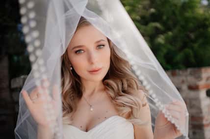 happy bride with long wavy hair under the veil outside. Wedding make-up. wedding planner's services. traditional wedding accessories and merchandise.decorative and caring cosmetics. Natural beauty