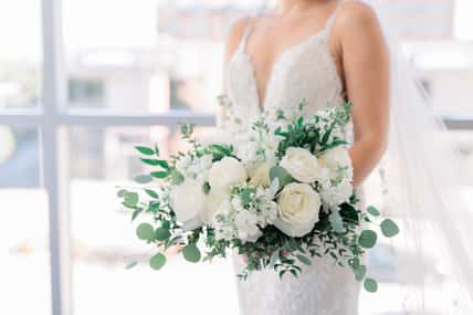 Bride is holding a white flower bouquet against her white wedding dress