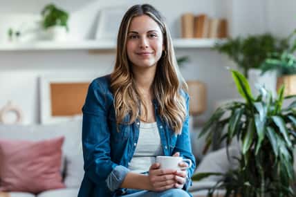 Shot of beautiful young woman drinking a cup of coffee while sitting on couch in living room at home.