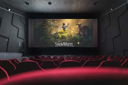 Movie theater screen displaying Disney Snow White film poster, viewed from empty red cinema seats. April 5, 2025