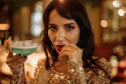 Beauty young brunette woman portrait with a glass drinking a cocktail at a bar look at the camera