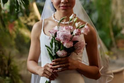 Closeup of young black woman as bride wearing wedding dress and holding delicate flower bouquet in pink tones, copy space
