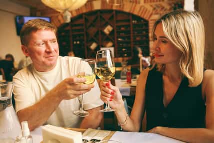 Cheers. Romantic young couple at restaurant raising a toast. Beautiful couple with glasses of white wine in restaurant. Couple toasting wine glasses during a romantic dinner in a gourmet restaurant.