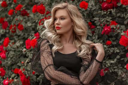 Beautiful blonde woman in garden with red roses. Spring time.