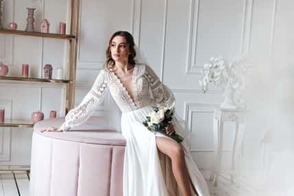 An attractive young bride in a beautiful boho wedding dress posing with a bouquet in a bright room. Wedding photo session, bride's morning.