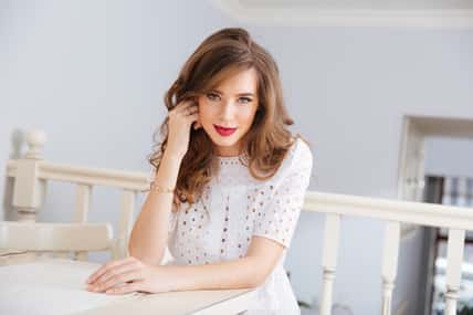 Portrait of attractive smiling young woman in white dress in cafe