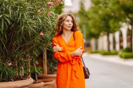 Cheerful tourist in a bright dress walks along a beautiful street. A young woman enjoys the weather outdoors. The concept of walking, vacation, travel. Active lifestyle.