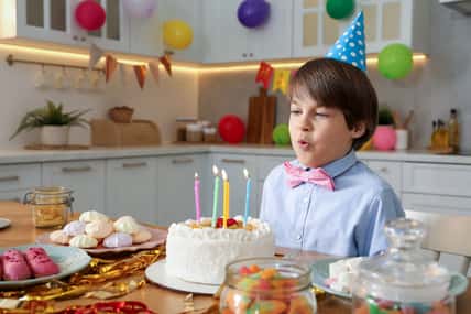 Cute little boy blowing out candles on birthday cake indoors. Surprise party
