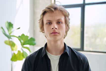 Headshot portrait of serious handsome teenager guy looking at camera, inside home living room. Teenage age, males 16-17 years old, adolescence, education, lifestyle, leisure concept