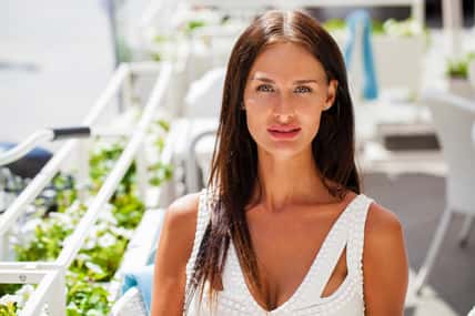 Young beautiful girl in white dress drinks coffee in summer restaurant