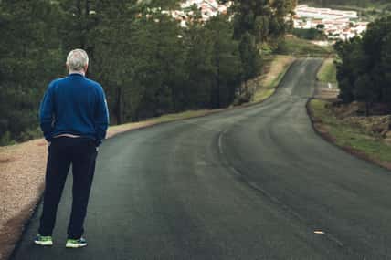 Active senior man standing on lonely road between mountains. Older man of back standing on lonely highway