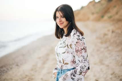 Stylish hipster girl walking on beach at sea. Calm portrait of happy fashionable boho woman relaxing at sandy cliff on tropical island. Travel and summer vacation. Space for text