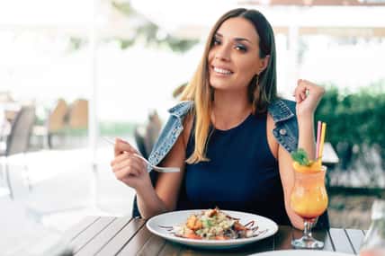 Beautiful young caucasian woman eating fresh caesar salad in an outdoor restaurant. Summer mood, enjoying food, happy people