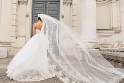 Wedding day. Bride in white wedding dress holding long veil with embroidery