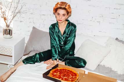 nice woman in pajamas doubting with pizza box in bed