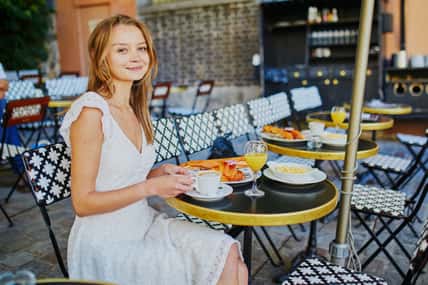 Cheerful young woman having breakfast or brunch in traditional French cafe on Montmartre in Paris, France