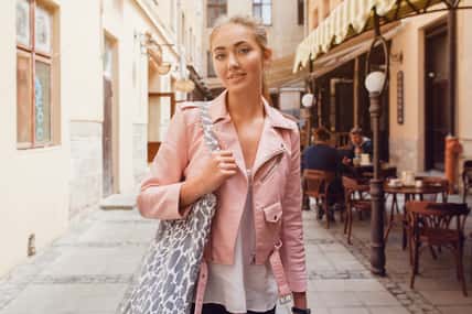 young beautiful woman traveling in europe, summer vacation, sunglasses, leather pink jacket, glam rock style, city street style, shopping bag