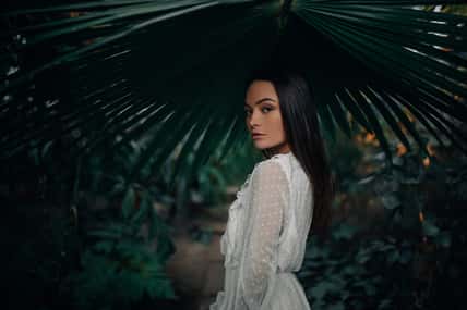 Portrait of young woman under big leaf of palm tree inside orangery.