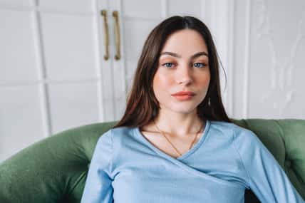 Portrait of attractive pretty young woman in casual clothing sitting on a sofa and looking on camera.