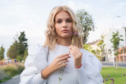 A portrait of a beautiful blond girl holding a purple flower close to her face.