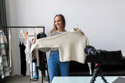 Fashion blogger woman in jeans and turtleneck showing casual colorful shirts on camera. Stylist influencer girl showing trendy clothes filming vlog episode for her channel. Opinion leader sets trends.