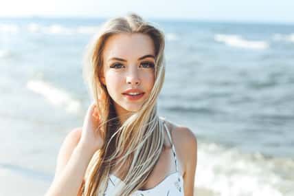Happy blonde woman in free happiness bliss on ocean beach standing straight and posing.