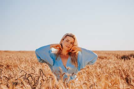 Beautiful adult blonde woman in summer in a field among ears of corn enjoys the warmth and fragrance of flowers - a portrait of a charming beauty