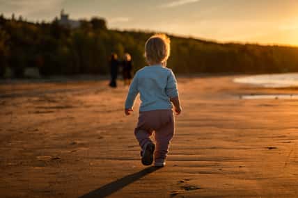 Little baby child toddler walks along an empty beach by the sea at sunset alone, calm and relax, active childhood