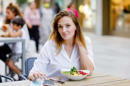 Young beautiful woman eating fresh salad in outdoor restaurant. Woman enjoying lunch bowl with fresh vegetables. Healthy food. On summer day