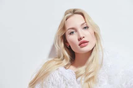 Portrait of a beautiful young woman with blonde hair and sensual lips posing in a fluffy white fur coat on a white studio background. Beauty care cosmetics. Cosmetology.