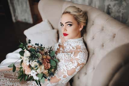 Beautiful bride in a lace dress with an original wedding bouquet in a vintage interior.