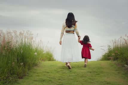 mother walking with her toddler girl on a grass field