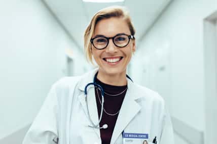 Portrait of happy young female doctor standing in hospital corridor. Caucasian woman working in healthcare center.