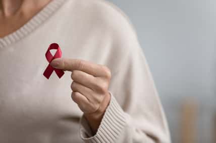 Close up of senior woman hold red ribbon breast cancer symbol support people patient with illness, middle-aged female volunteer keep AIDS HIV disease awareness, elderly healthcare, medicine concept