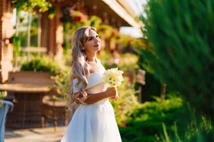 beautiful blonde bride with a bouquet of callas on the path in the garden. wedding in the park. the concept of choosing a place for the celebration.